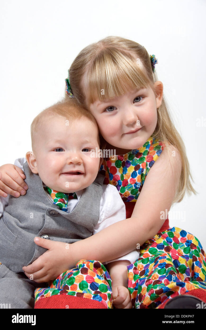Kleine Mädchen und Baby Bruder sitzt zusammen kuscheln sowohl elegant gekleidet in Anzug und Krawatte und passende nicht so Doll Kleid, UK Stockfoto