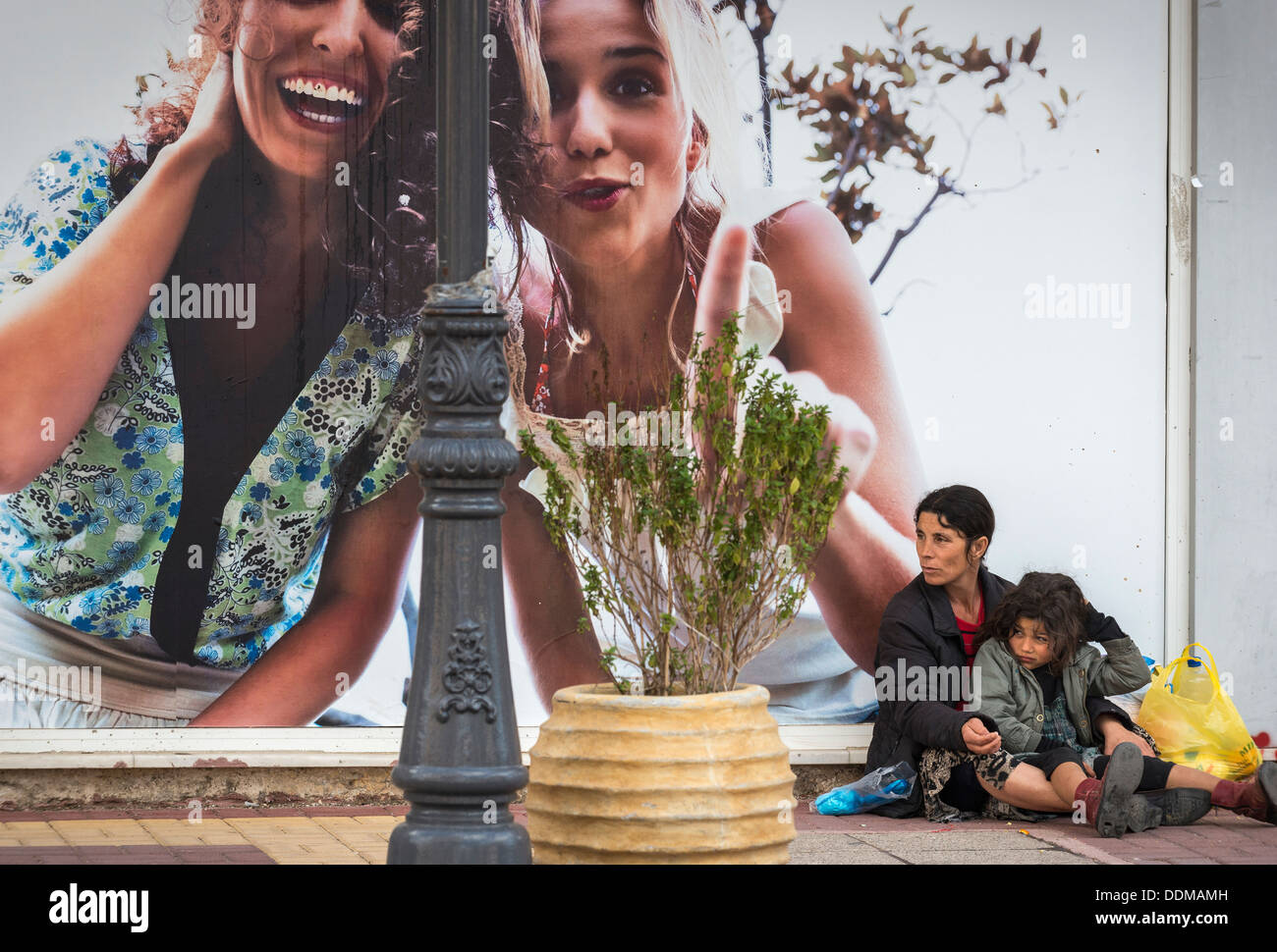 Roma-Frau und Kind betteln neben einer Werbung Horten in der provinziellen Stadt Zacharo, Peloponnes, Griechenland Stockfoto