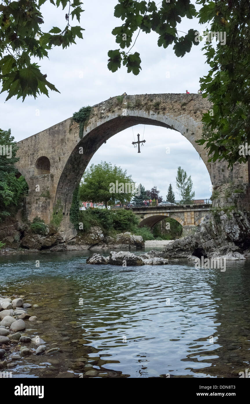 Cangas De Onis, Asturien, Spanien. Die römische Brücke am Fluss Sella, ein Victoria-Kreuz hängt von der Brücke. Stockfoto