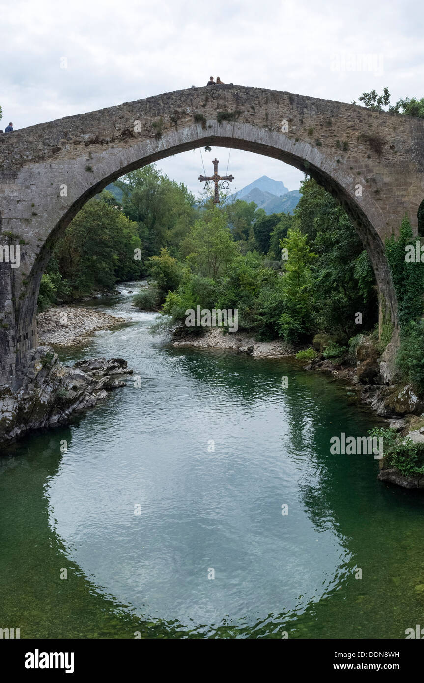Cangas De Onis, Asturien, Spanien. Die römische Brücke am Fluss Sella, ein Victoria-Kreuz hängt von der Brücke. Stockfoto