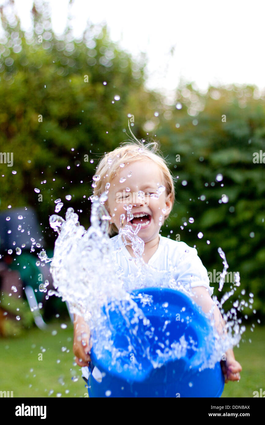 Blondes Mädchen mit Spalshing mit Wasser im Garten Stockfoto