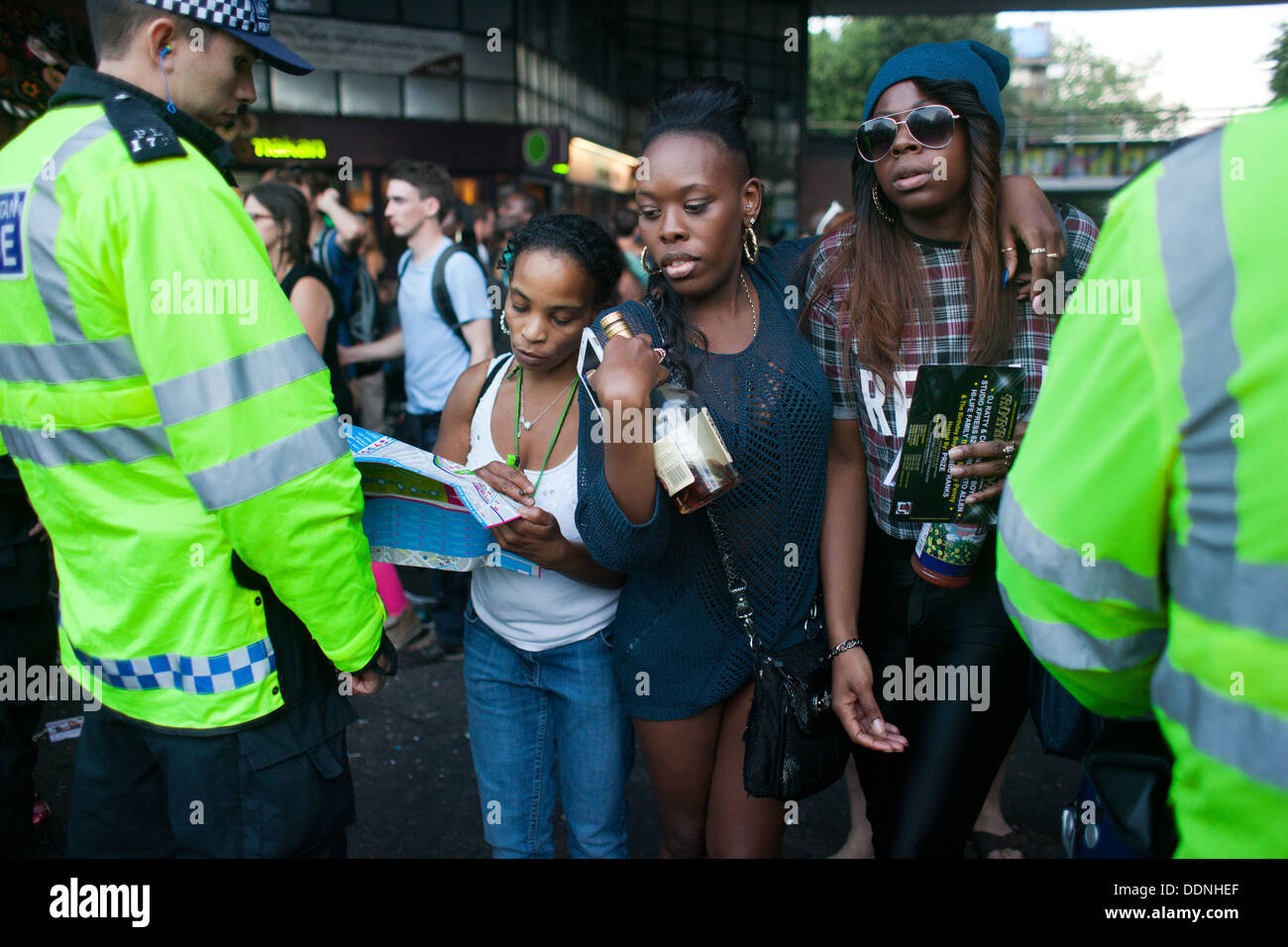Eine Frau bitten um Richtung, wie zwei junge schwarze Mädchen mit einer Flasche Ofwhiskey in ihren Händen ihren Weg durch die Polizeilinien schieben. Stockfoto
