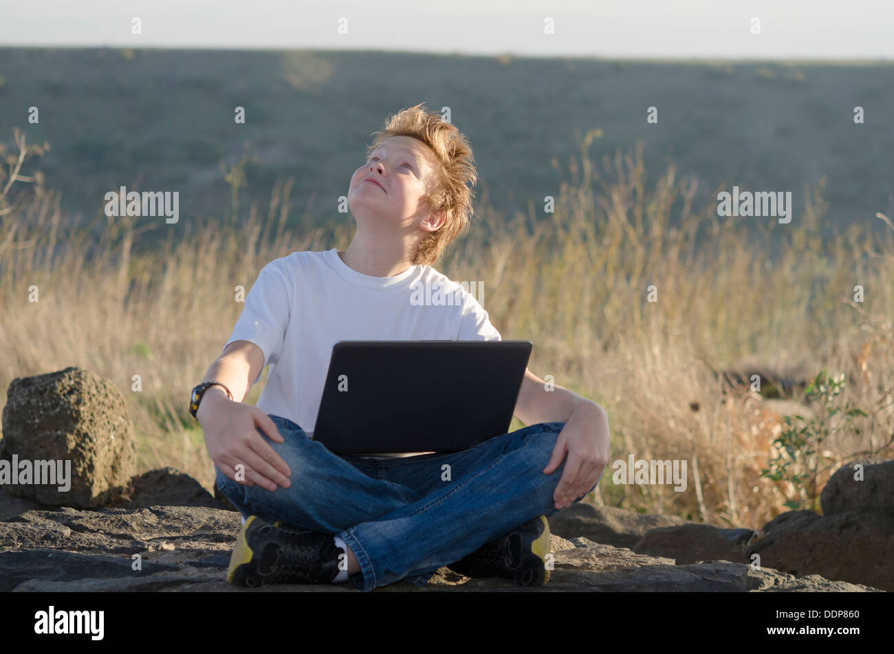 Hübscher Junge mit Laptop sitzt in der Natur und der Blick in den Himmel Stockfoto