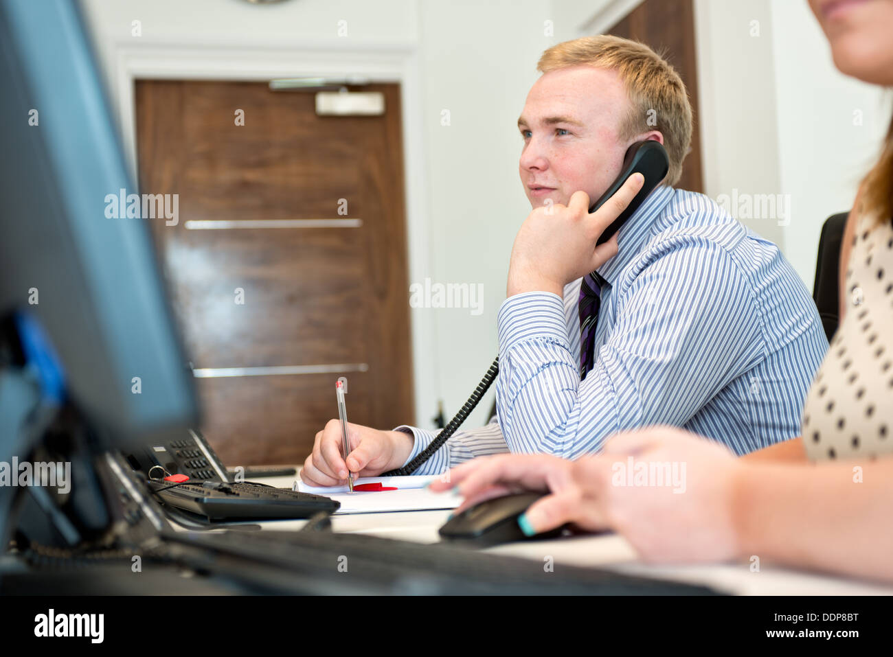 Eine junge männliche Büroangestellte konzentrieren, telefonieren & Arbeit mit einem Computer in einer modernen Büroumgebung Stockfoto