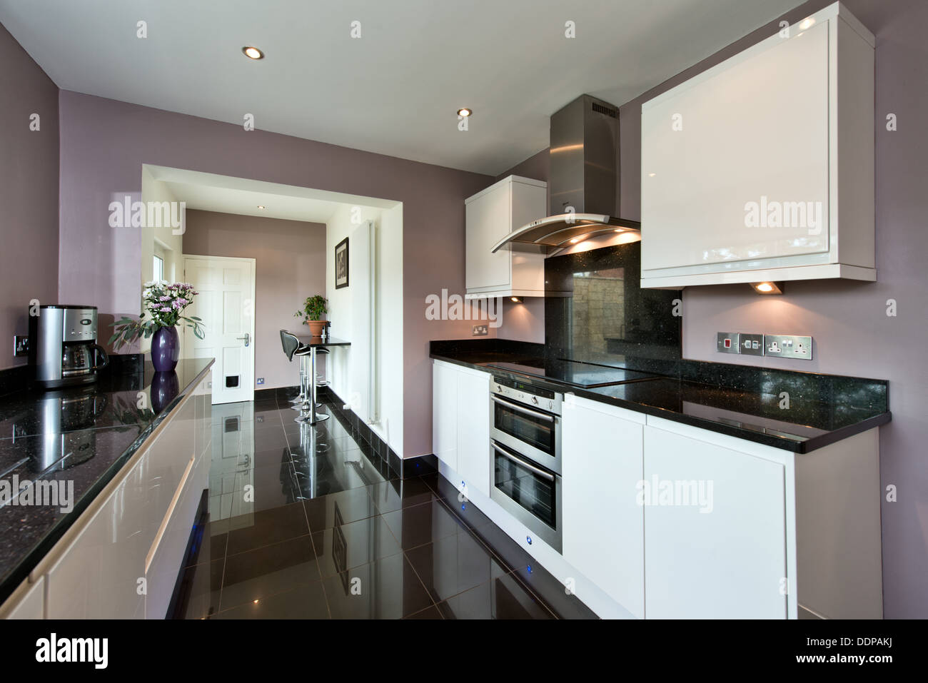 Eine installierte saubere moderne Designer-Küche in Hochglanz weiß mit schwarzer Granitarbeitsplatte und Bodenfliesen Stockfoto