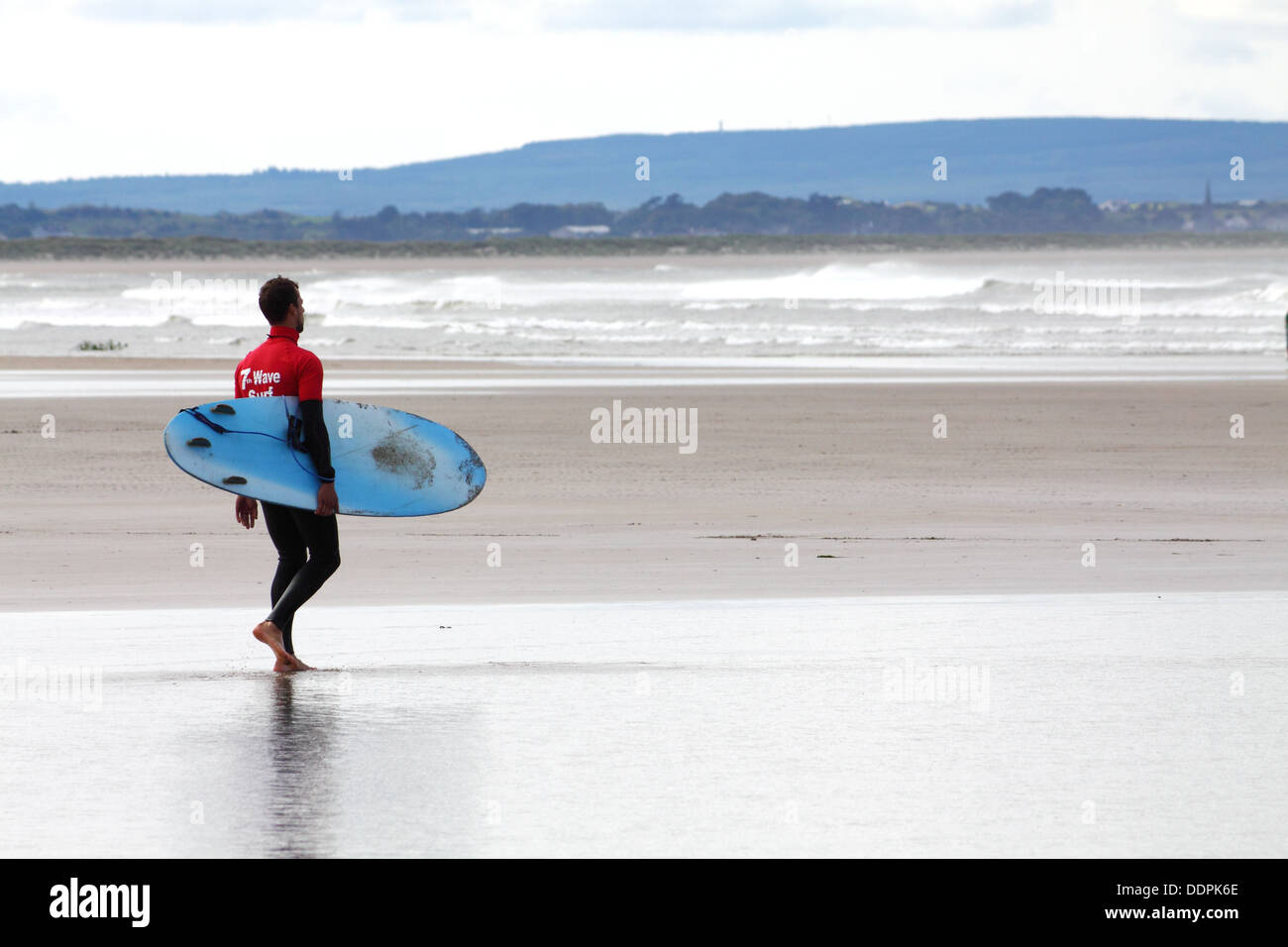 Surfer mit Surfbrett zu Fuß am Strand von Enniscrone, Irland Stockfoto