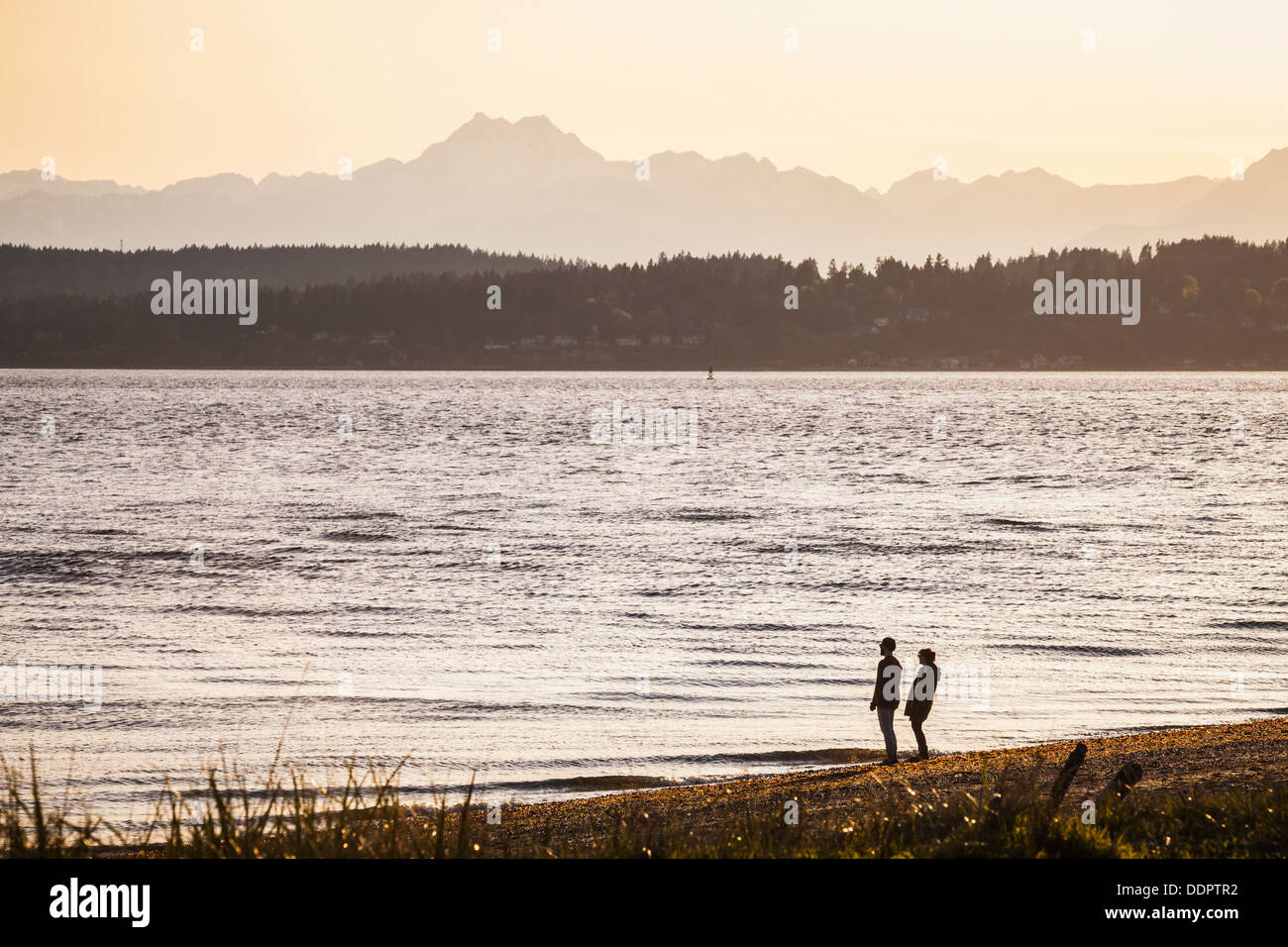 Ein Mann und eine Frau stehen am Strand, Blick auf den Puget Sound und die Olympic Mountains im Discovery Park in Seattle Wa Stockfoto