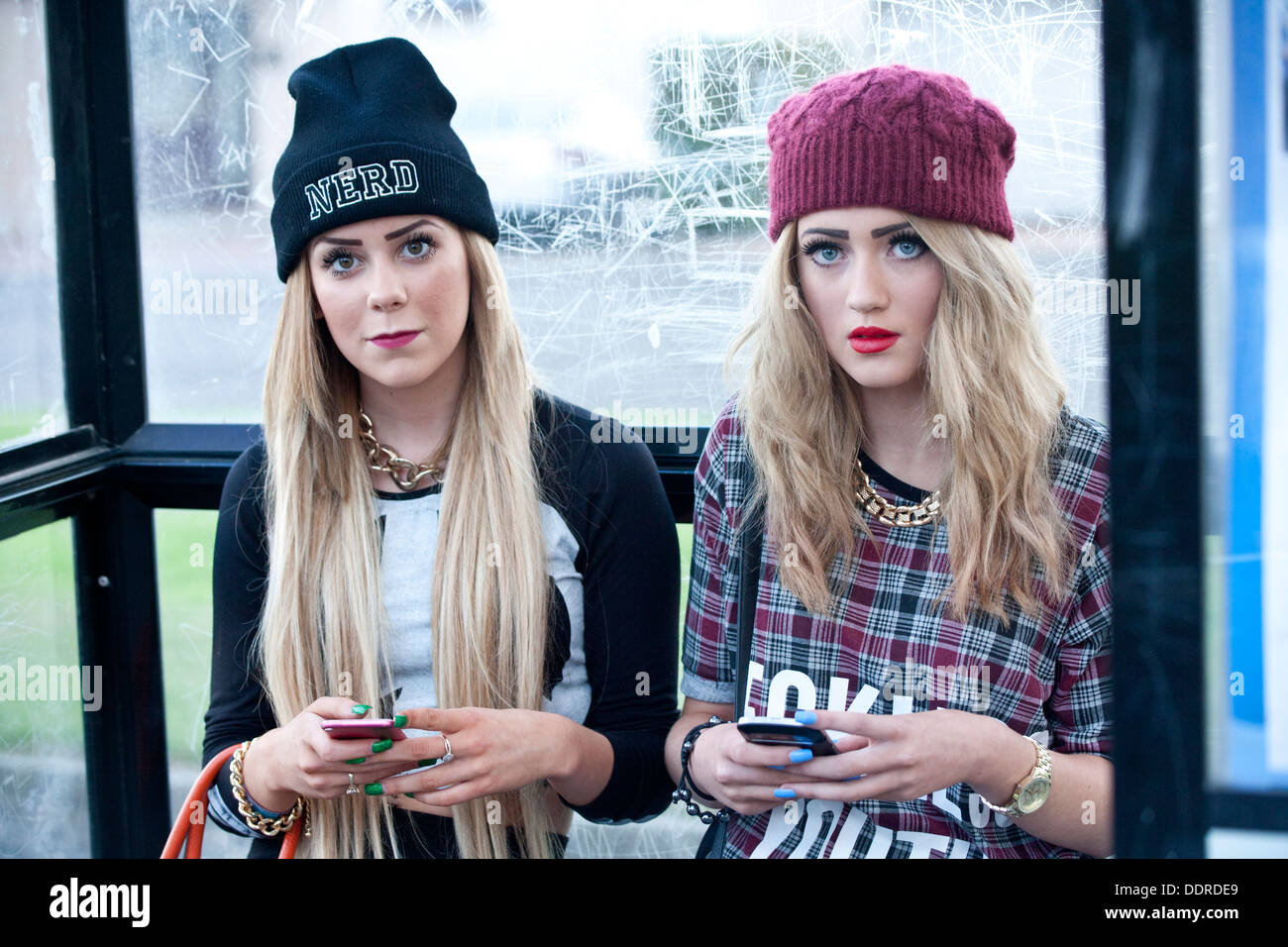 Zwei Mädchen im Teenageralter sitzen im Bus stop halten Handys. Stockfoto