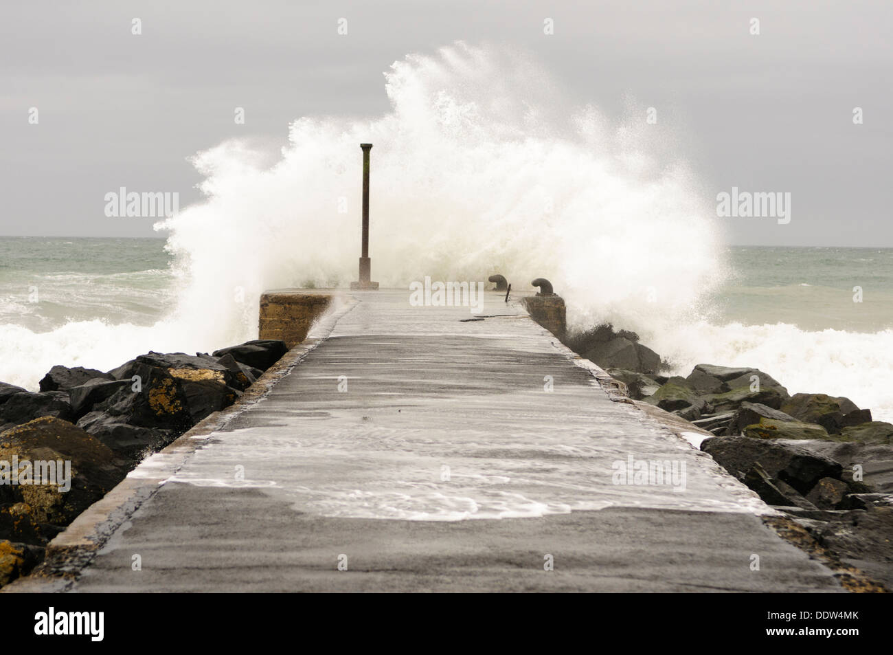 Eine Welle stürzt über das Ende von einem Pier in windigen Bedingungen Stockfoto