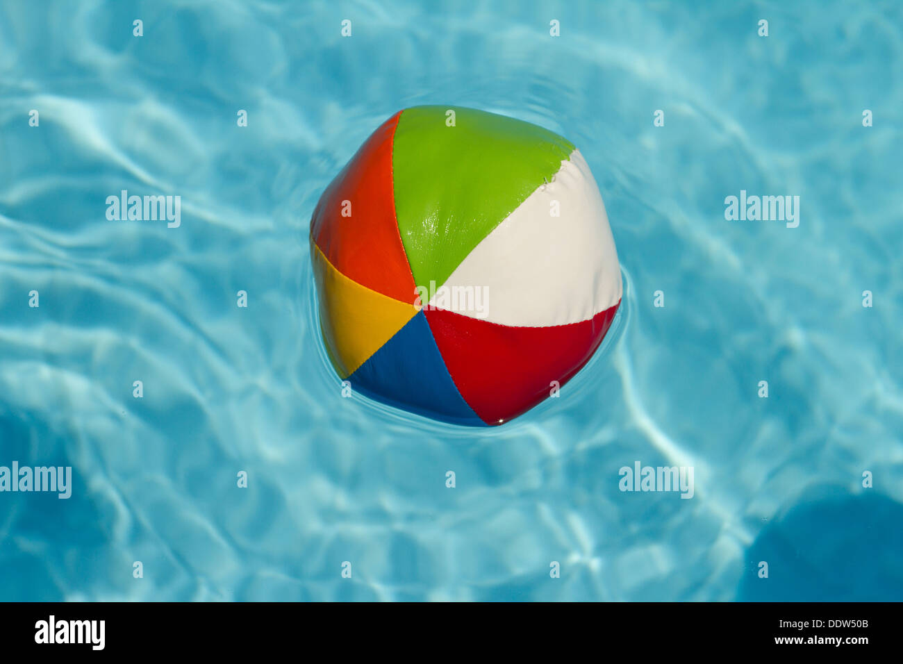 Einen bunten Wasserball schwebend in einem leuchtend blauen Swimmingpool. Stockfoto