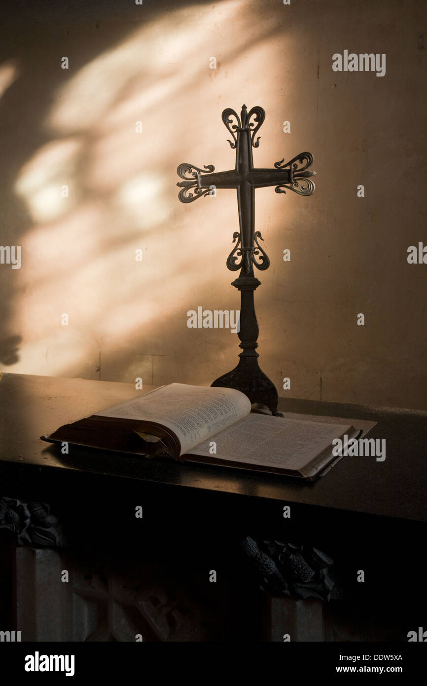 Detail aus dem Inneren einer Kirche mit einem dekorativen Kreuz auf ein Stativ und Bibel auf Tisch, beleuchtet aus Glas Seitenfenster. Stockfoto