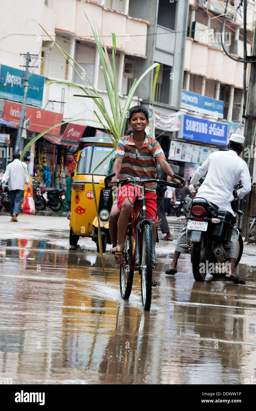 Indischen jungen Fahrrad durch eine Pfütze im Regen mit Zuckerrohr. Puttaparthi, Andhra Pradesh, Indien Stockfoto