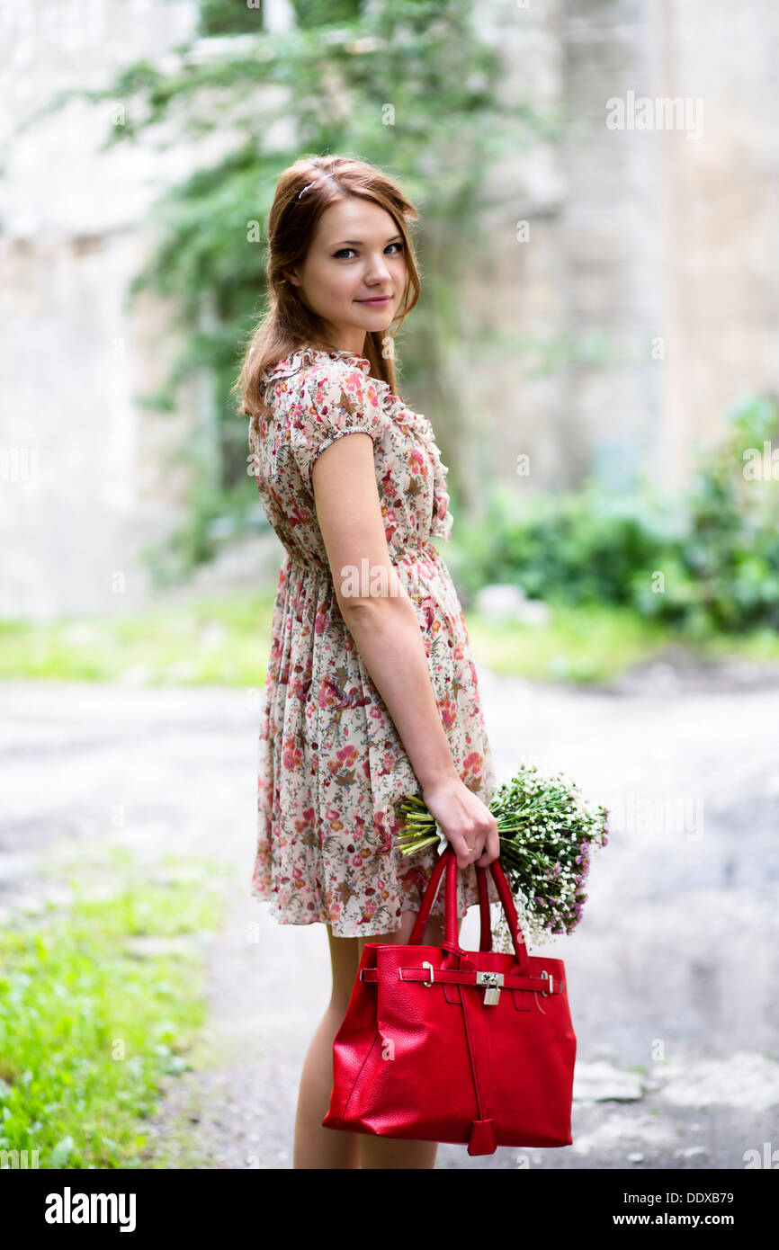 Frau im geblümten Kleid halten Blumen und Tasche Stockfoto
