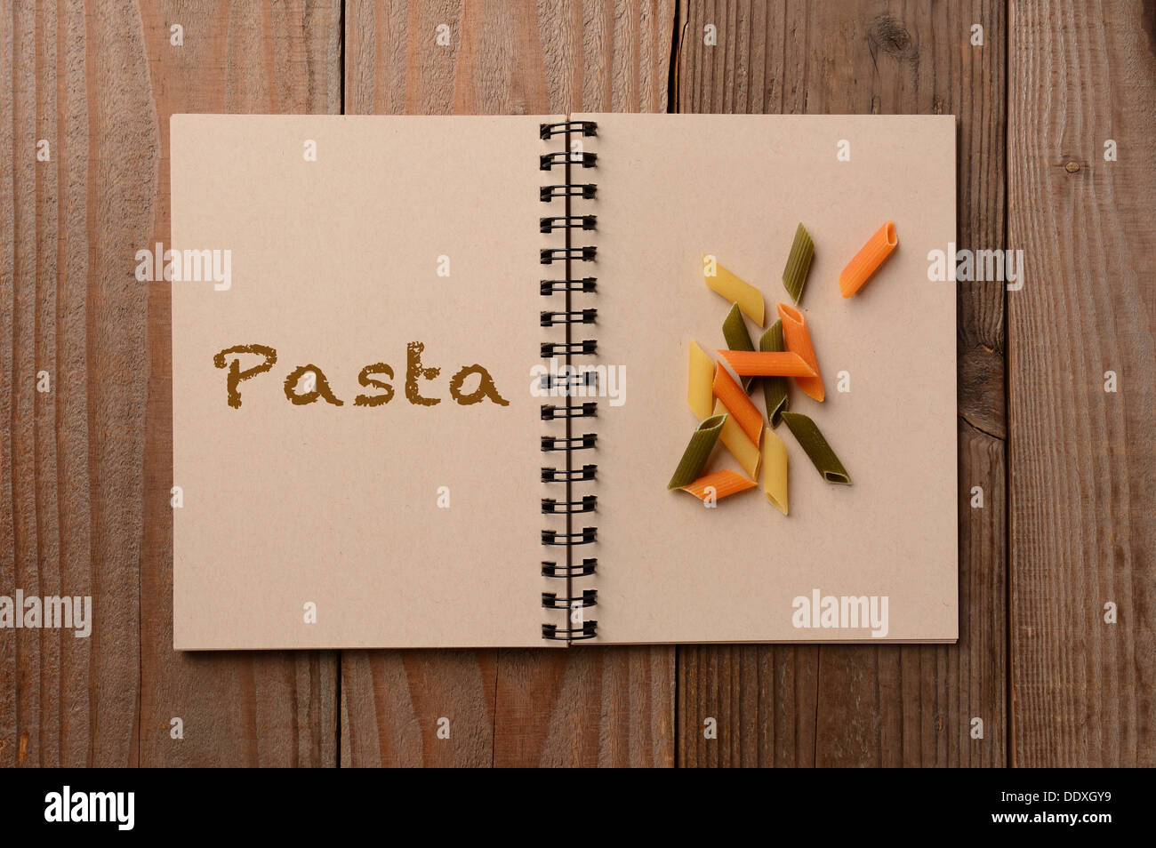Eine Gruppe von bunten Pasta auf die leere Seite eines Notebooks. Der gegenüberliegende Seite hat das Wort, die, das Pasta ausgeschrieben. Stockfoto