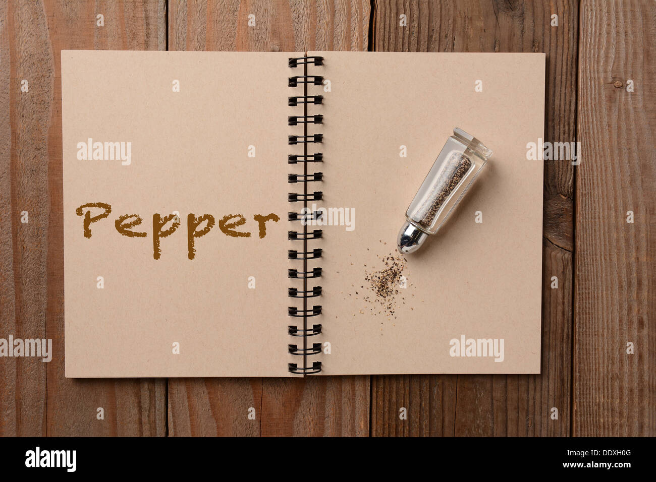 Ein Pfefferstreuer auf die leere Seite eines Notebooks. Der gegenüberliegende Seite hat den Wort Pfeffer ausgeschrieben. Stockfoto