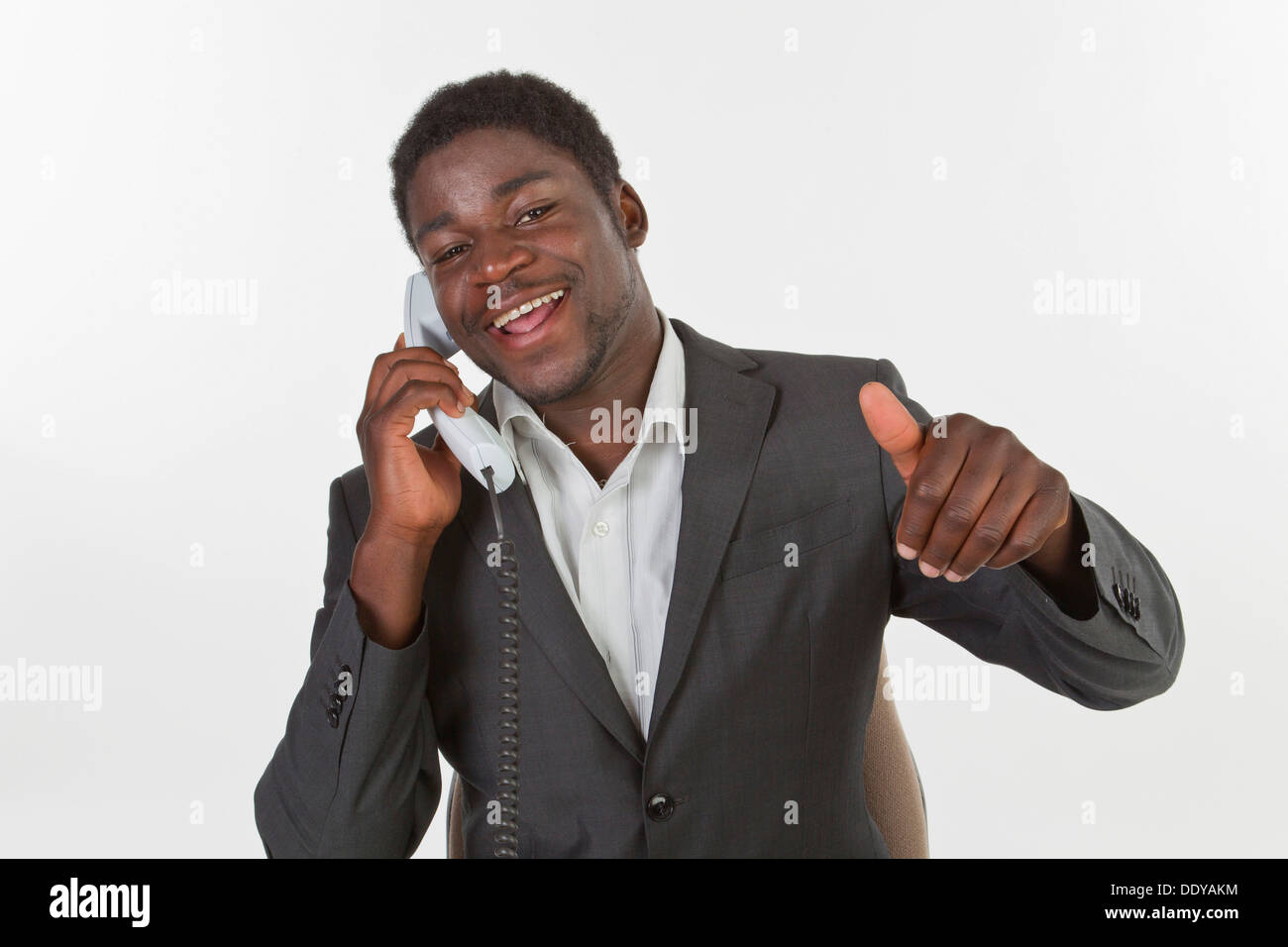 Junge schwarze Mann in einem Anzug, einen Anruf zu tätigen, in einem Büro, lächelnd mit einem Daumen hoch Geste Stockfoto