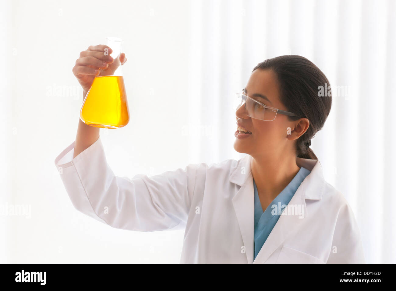 Junge Wissenschaftlerin Blick auf gelbe Flüssigkeit im Becherglas Stockfoto