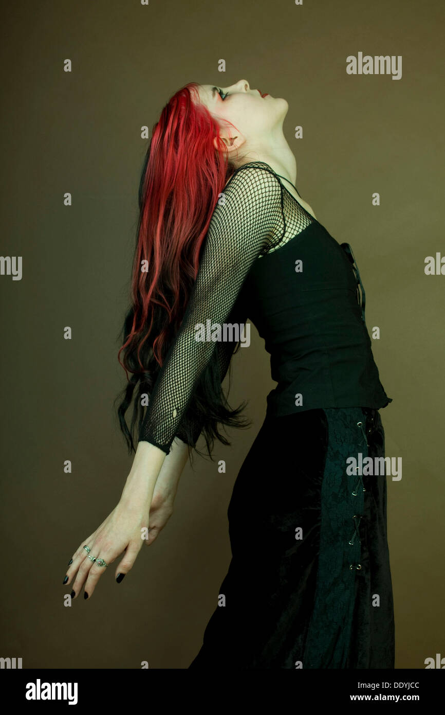 Frau mit roten Streifen im Haar Goth Subkultur, stehend mit ihren Armen zurück gebogen Stockfoto
