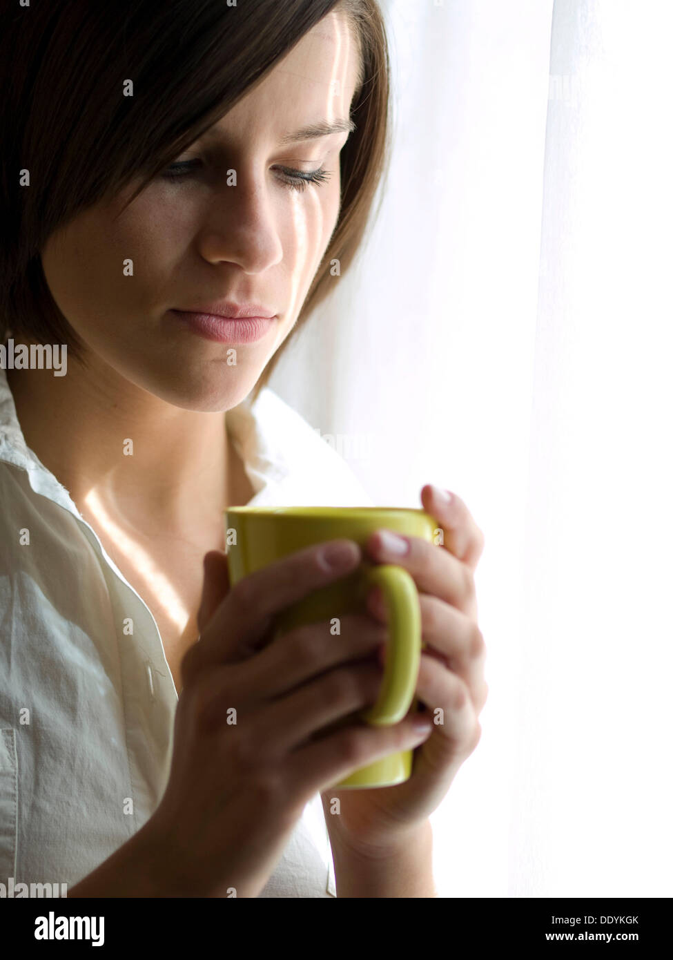 Junge Frau mit einer Tasse Kaffee, steht man vor einem Fenster Stockfoto