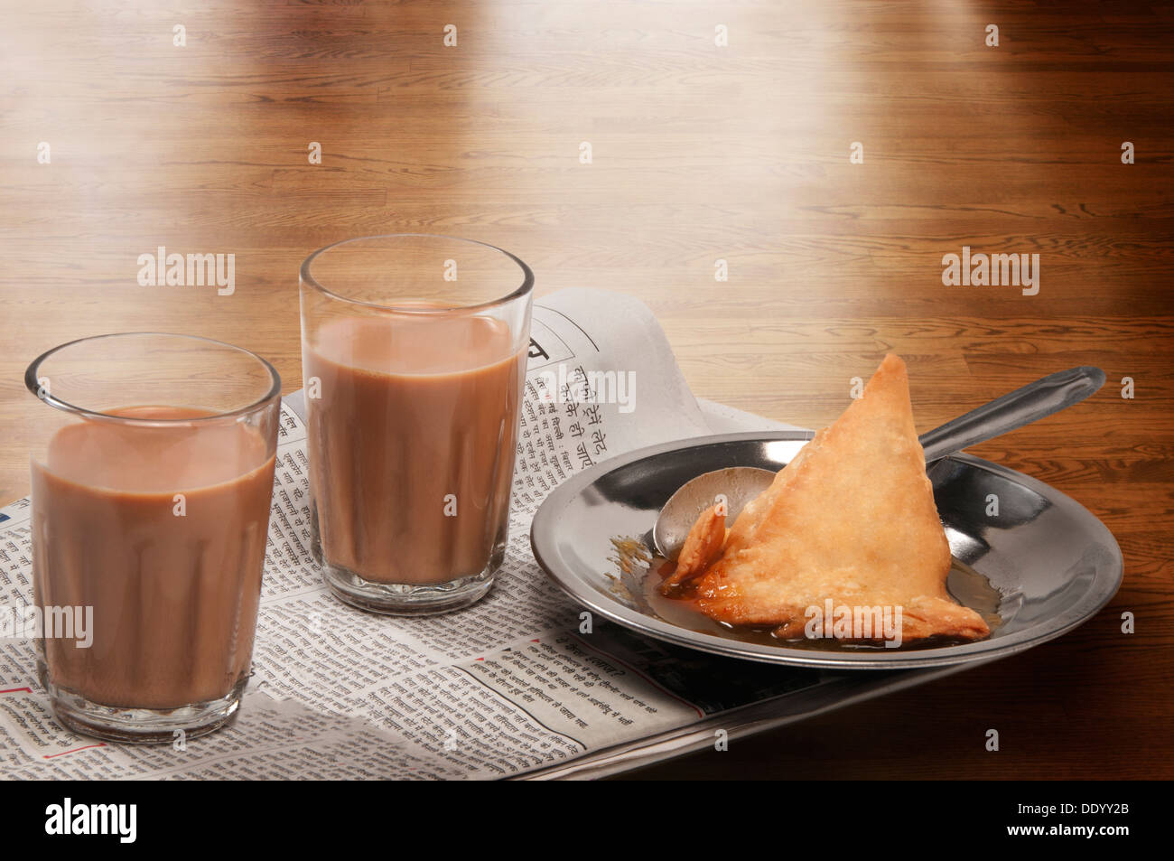 Brille von Chai auf Zeitungspapier mit Teller Samosa über eine Holzoberfläche Stockfoto