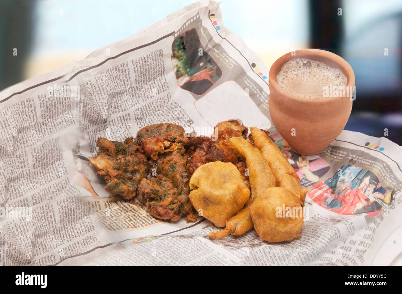 Indische Pakoras, Bhajiyas und frittierten Kartoffelbällchen mit Chai in traditionellen Tasse aus Schlamm auf einer Zeitung Stockfoto