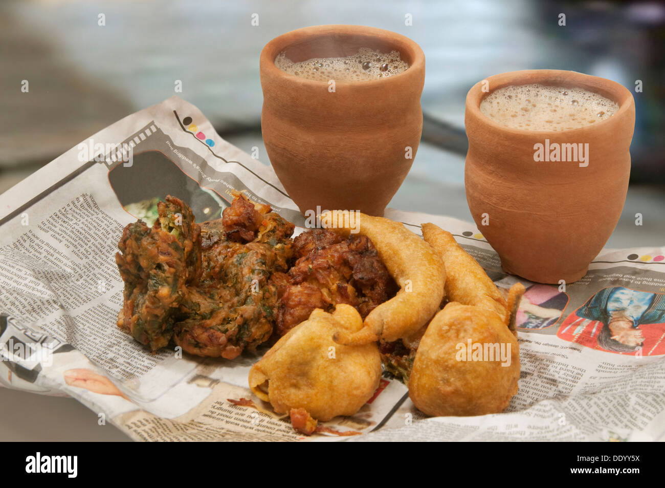 Indische Pakoras, Bhajiyas und frittierten Kartoffelbällchen mit Chai in traditionellen Tasse aus Schlamm auf einer Zeitung Stockfoto
