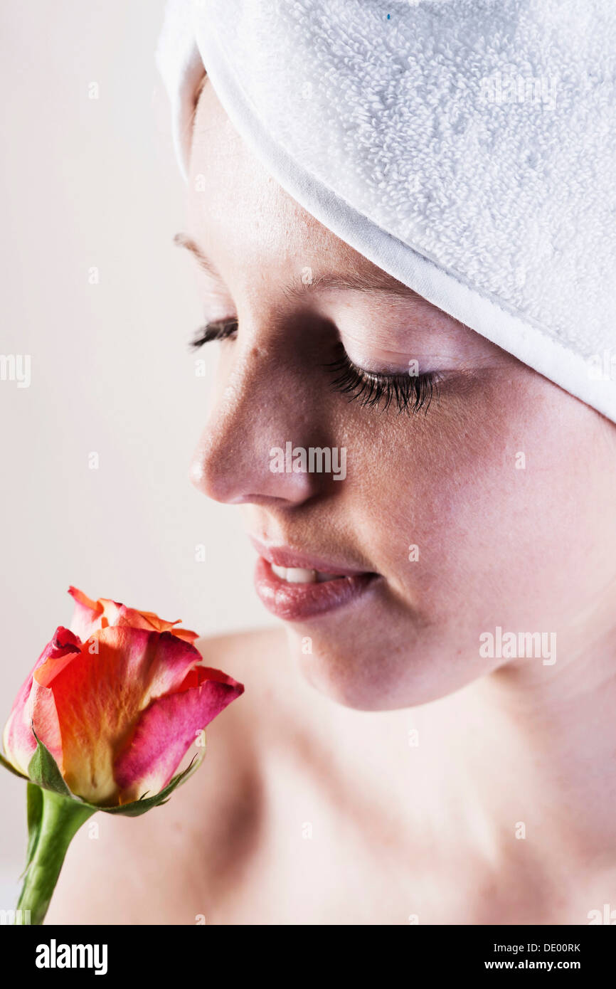 Porträt einer lächelnden jungen Frau riechen eine Rose mit einem Handtuch um den Kopf gewickelt Stockfoto