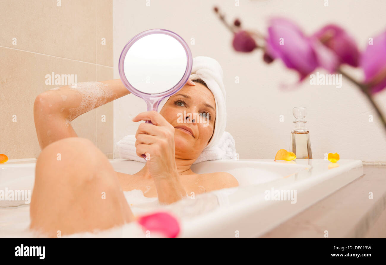Frau, die ein Bad zu nehmen und ihr Gesicht mit einem Spiegel zu betrachten Stockfoto