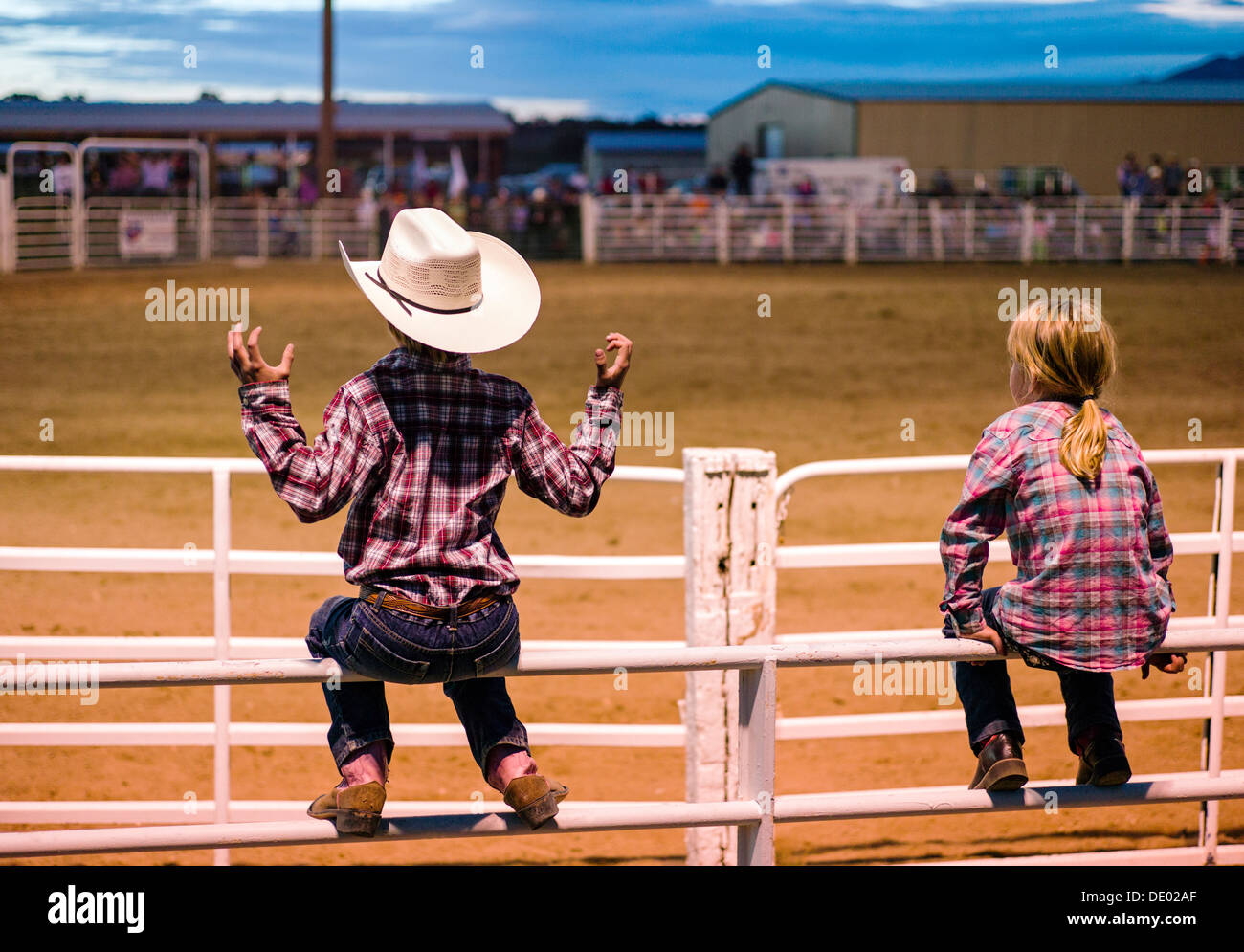 Junge & Mädchen gehockt Corral Zaun beobachten das Chaffee County Rodeo, Poncha Springs, Colorado, USA Stockfoto