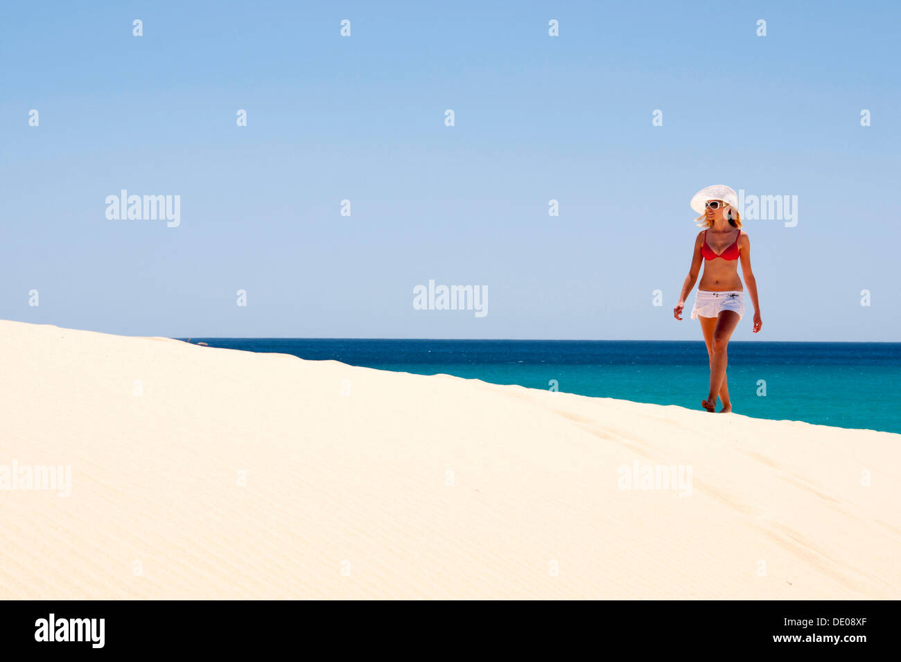 Frau trägt einen Hut und einen Bikini an einem Sandstrand zu Fuß Stockfoto