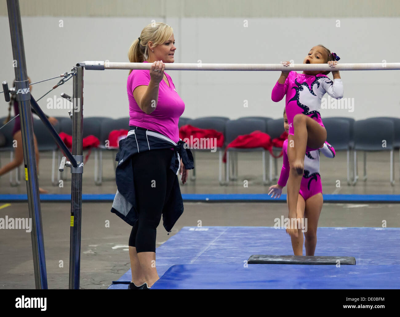 Detroit, Michigan - Trainer beobachtet, wie Mädchen am Barren vor Wettbewerb bei den Olympischen Spielen in AAU Junior Aufwärmen. Stockfoto
