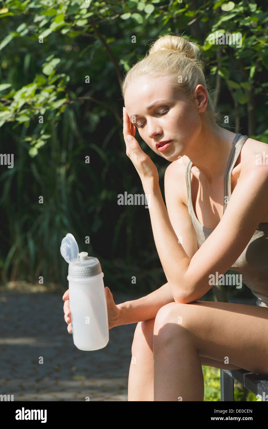 Junge Frau sitzt im Freien mit Wasserflasche, Augen geschlossen Stockfoto