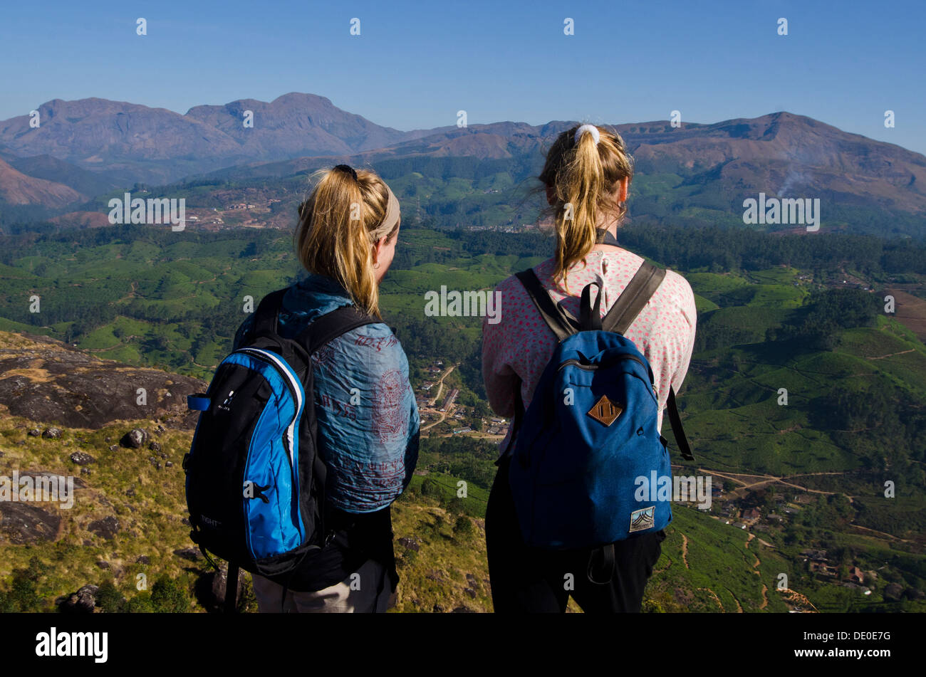 Zwei junge weibliche Touristen betrachten der Gebirgszüge von oben auf den Teeplantagen, Munnar, Kerala, Südindien. Stockfoto