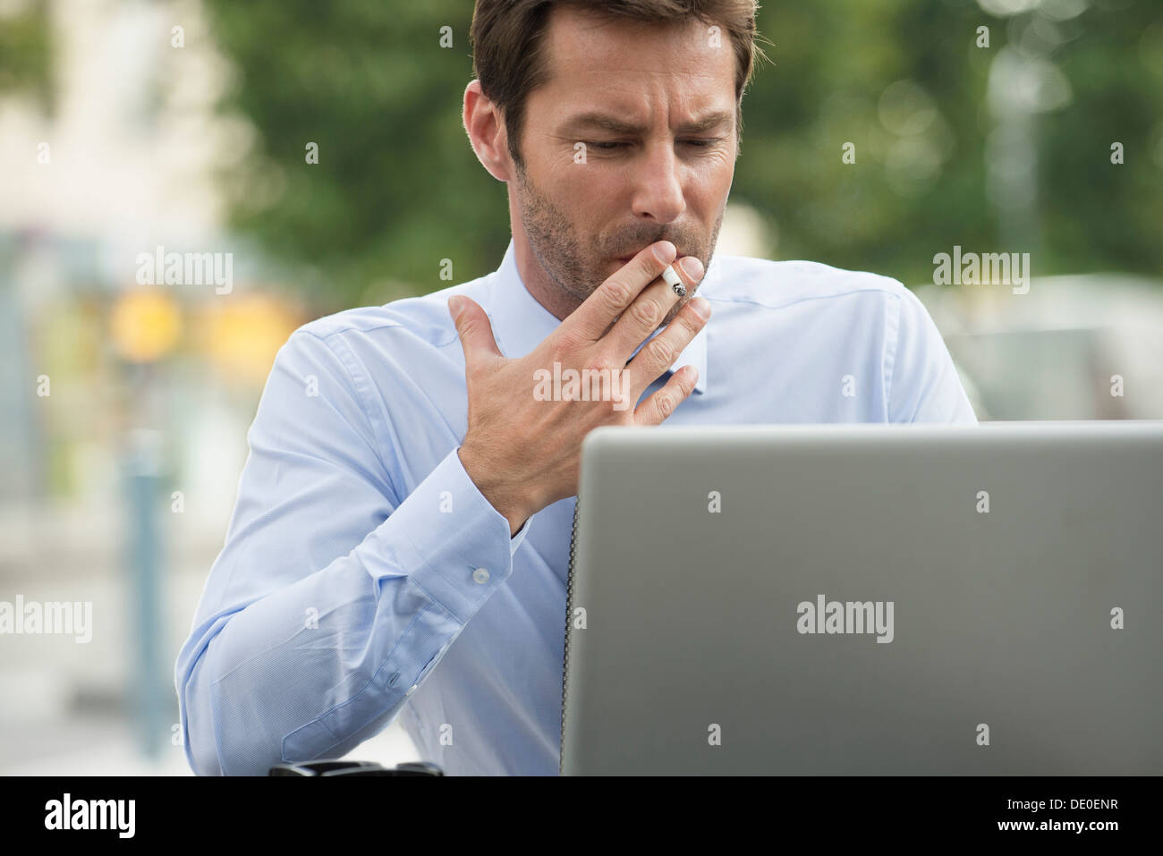 Geschäftsmann mit Laptopcomputer im Freien rauchen Stockfoto