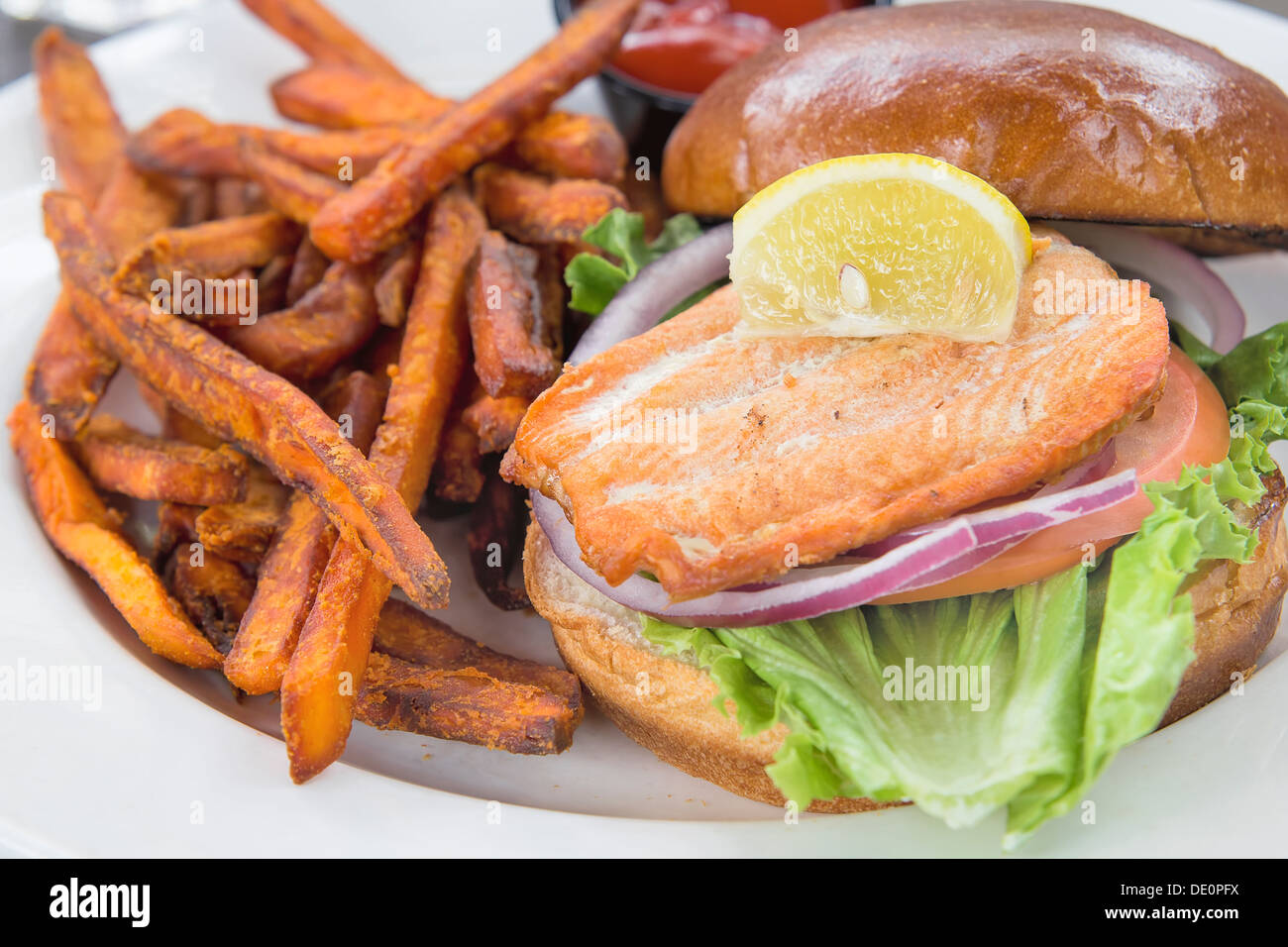 Lachs Fisch Steak-Sandwich mit Zwiebel-Tomaten-Salat und Süßkartoffel Pommes frites Closeup Stockfoto