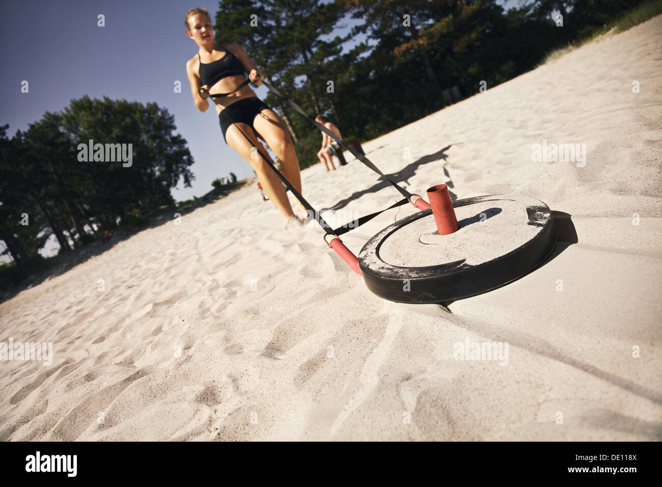 Starke junge Frau zieht einen Crossfit-Schlitten über einen Sandstrand im Freien an einem heißen Sommertag Stockfoto
