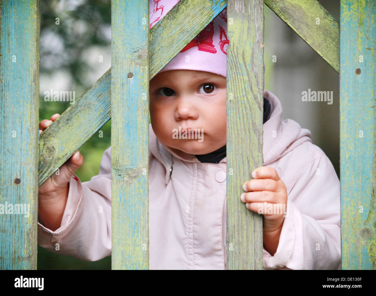 Brown eyed Babymädchen in rosa Hut spielt mit alten grünen hölzernen wicket Stockfoto