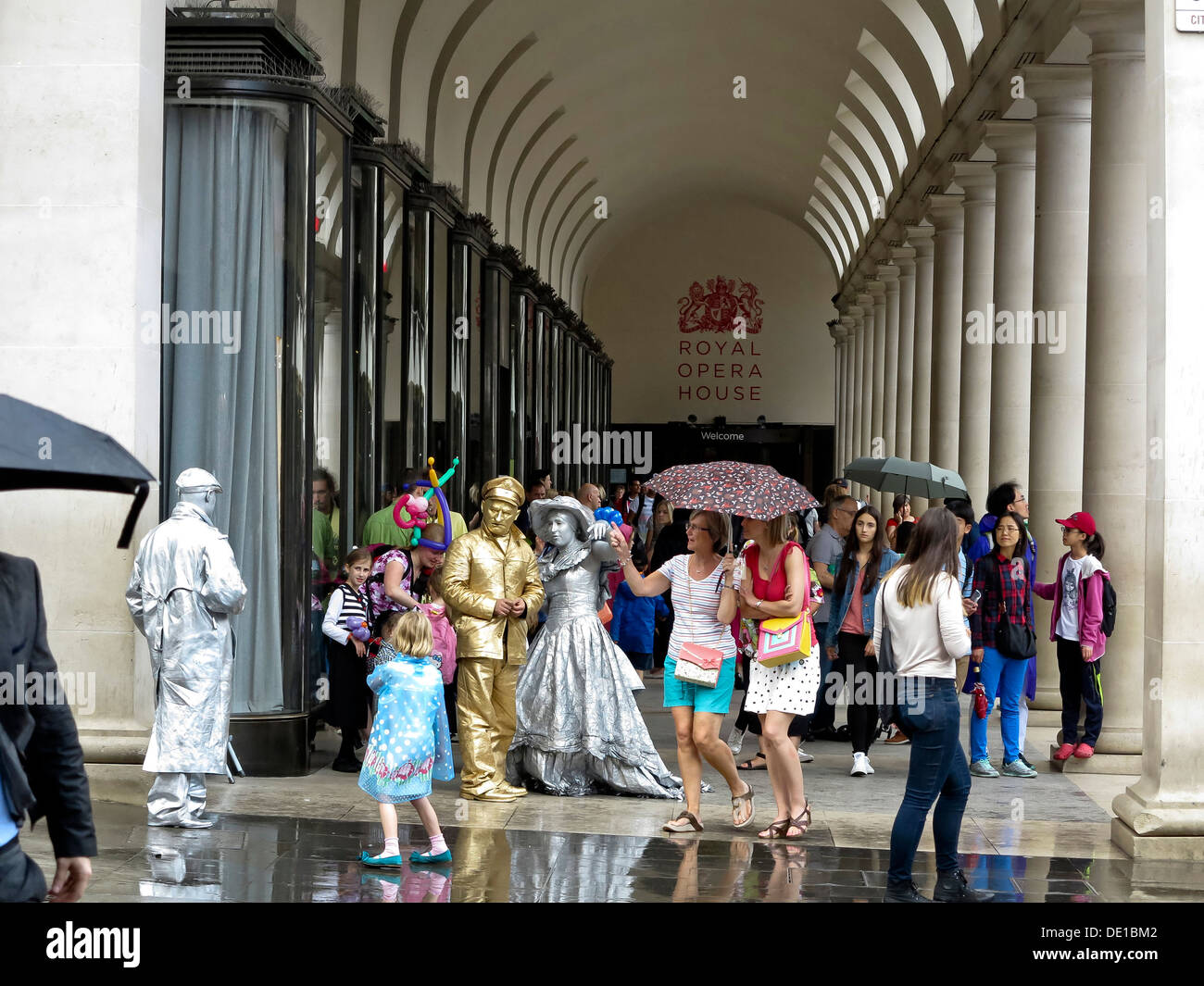 Touristen und "Menschliche Statuen" Schutz vor dem englischen Regen in der Nähe von The Royal Opera House in Covent Garden, London, UK Stockfoto