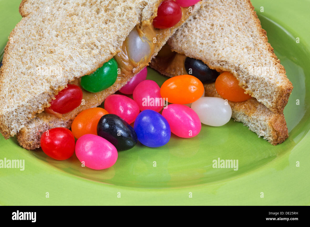 Eine Nahaufnahme eines Erdnussbutter und Marmelade Sandwich Bohne auf einer grünen Platte mit zusätzlichen Gummibärchen. Stockfoto