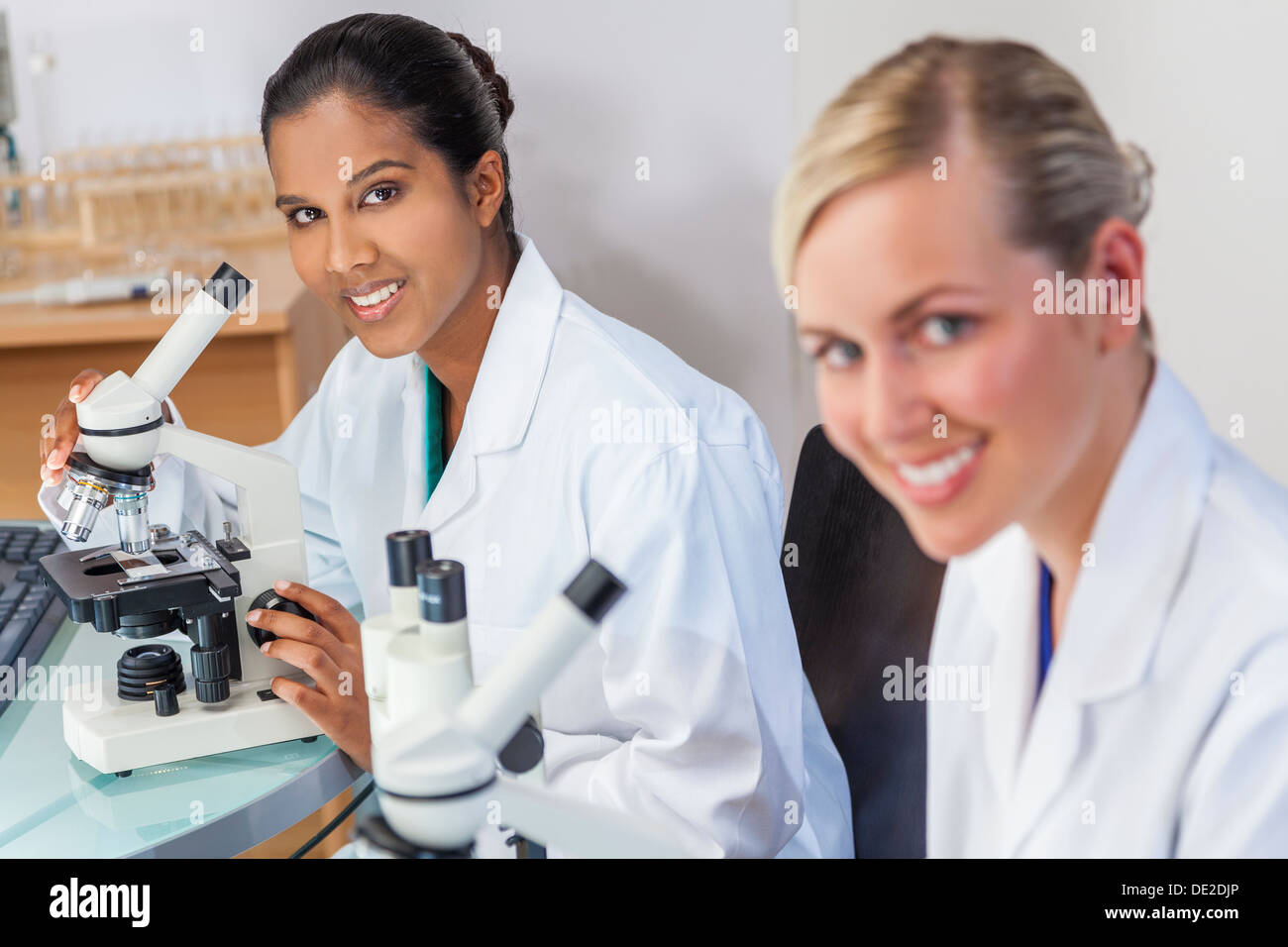 Eine indische asiatische medizinische oder wissenschaftliche Forscherin oder Arzt mit ihrem Mikroskop im Labor mit ihrer Kollegin. Stockfoto