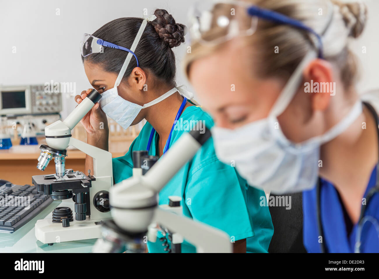 Eine asiatische medizinische oder wissenschaftliche Forscher oder Arzt mit ihrem Mikroskop im Labor mit ihrer Kollegin Stockfoto