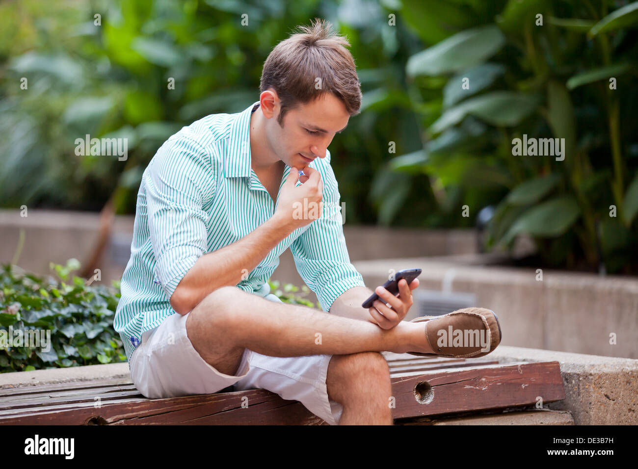 Mann sitzt im Garten mit einem Smartphone Stockfoto