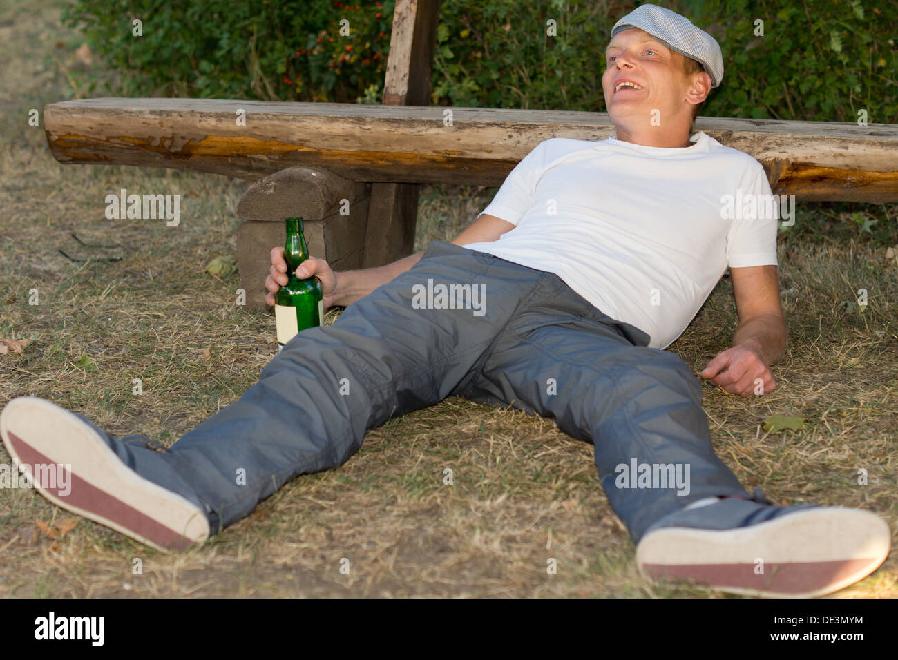 Betrunkener Mann erleben Euphorie durch übermäßigen Alkoholkonsum verursacht liegend im Park stützte sich auf eine Bank im park Stockfoto