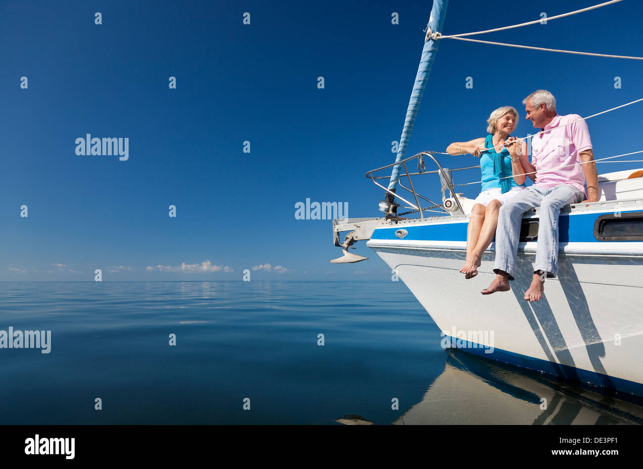Ein glückliches senior paar sitzt auf der Vorderseite eines Segelbootes auf einem ruhigen blauen Meer Stockfoto