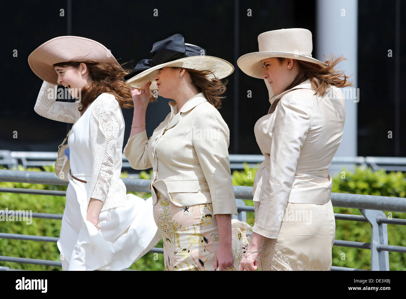 Ascot, UK, elegant gekleidet Frauen Halt bei starkem Wind Huete ihren festen Stockfoto