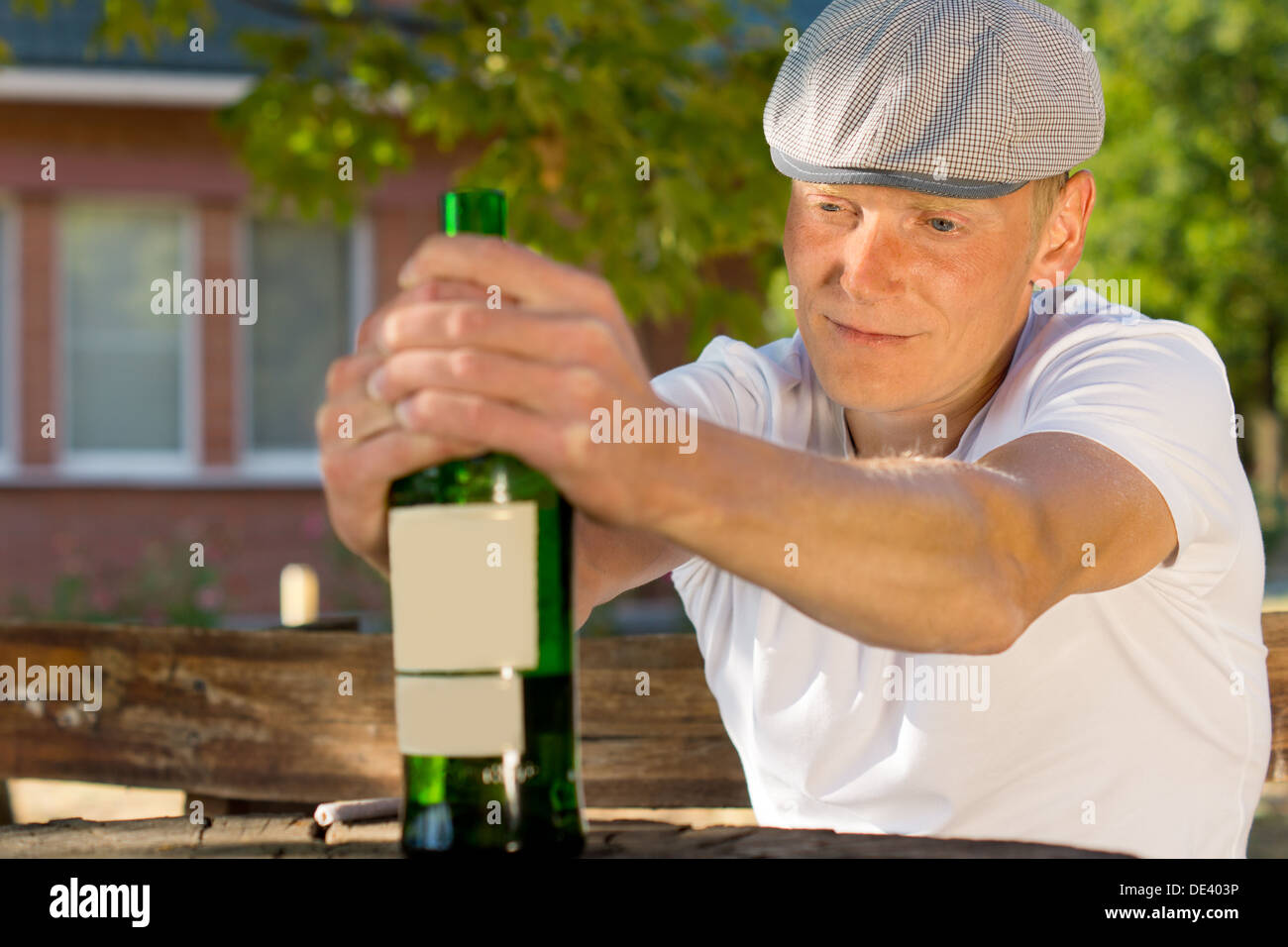 Alkoholische Mann schwindelig, sitzen an einem Tisch im Freien mit einer Flasche Wein Stockfoto