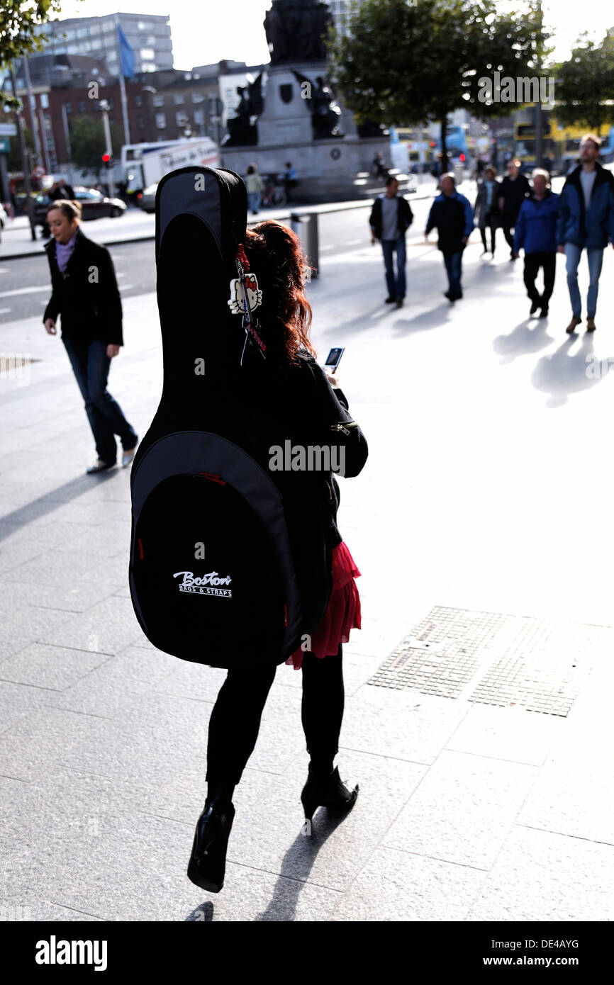 Irin, die Benutzung eines Mobiltelefons mit A Double Base Cello Musikinstrument auf dem Rücken, Dublin Irland Stockfoto