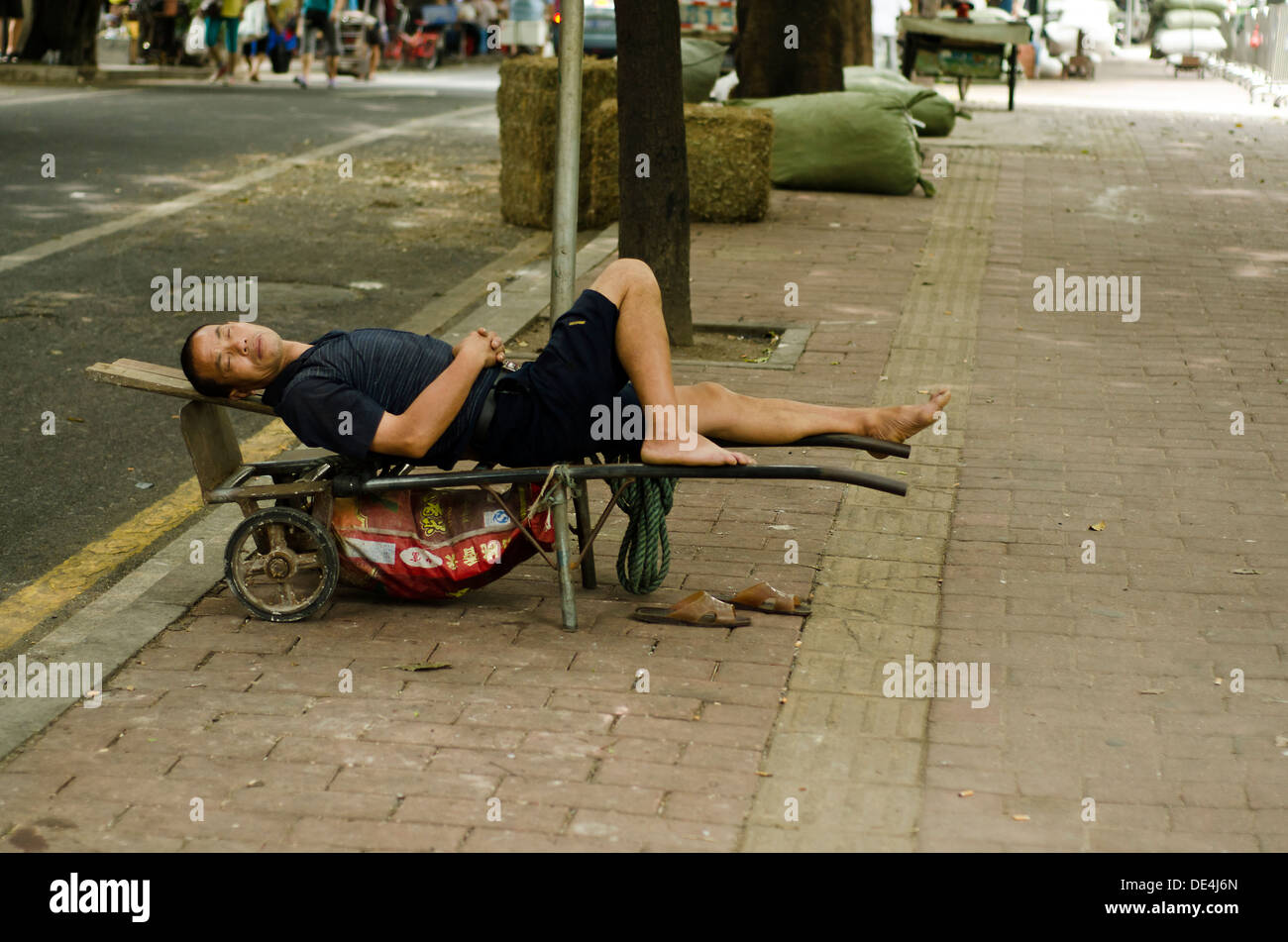 Chinesische Warenkorb Puller schläft am Straßenrand in der Mittagspause, Guangzhou, China Stockfoto