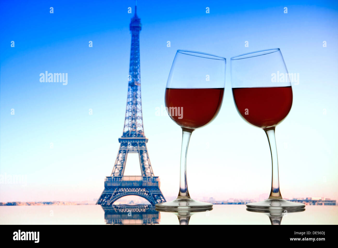 "Cheers" mit zwei Rotweingläser Neigung zu einander auf Café Glastisch mit Eiffelturm hinter Paris Frankreich Stockfoto