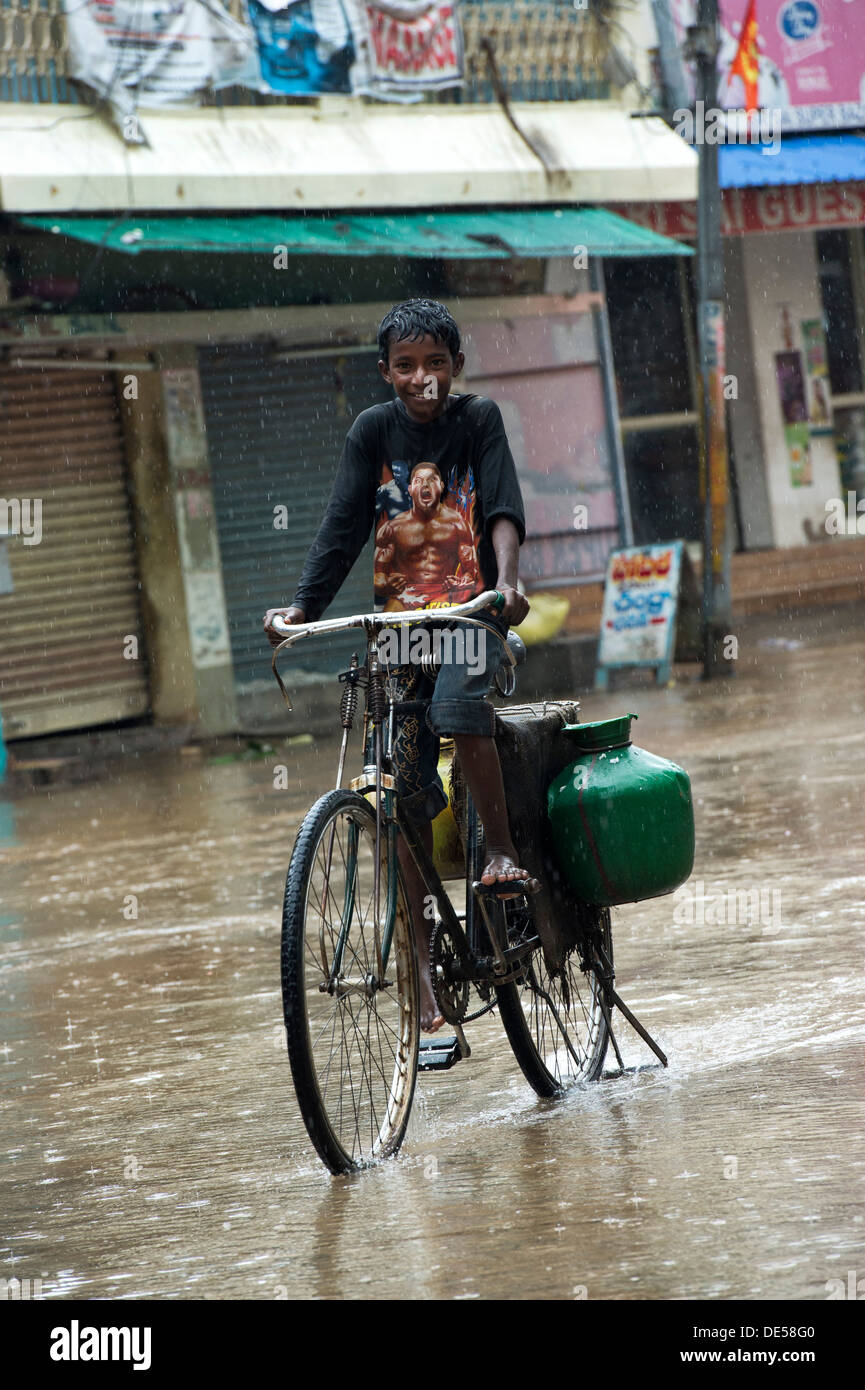 Niedrigen Kaste Indianerdorf junge Radfahren durch eine überschwemmte Straße während des Monsuns. Puttaparthi, Andhra Pradesh, Indien Stockfoto